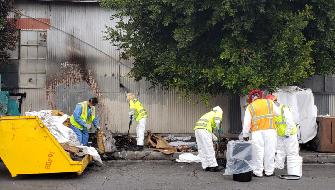 LASAN workers in protective clothing picking up trash on the street
