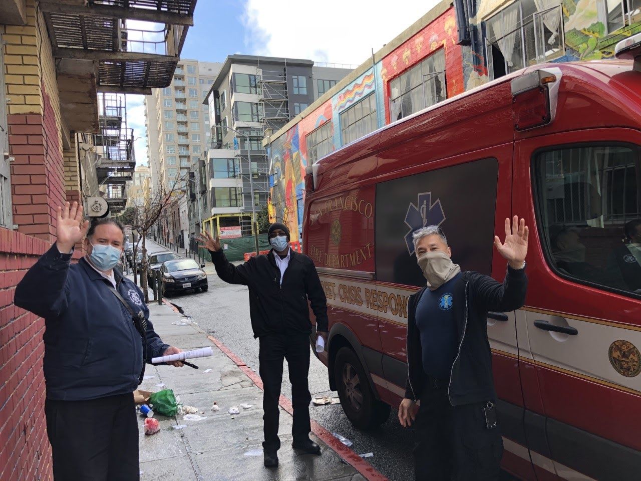 Three members of the SF Street Crisis Response Team in front of a city van, wearing masks and waving to the camera