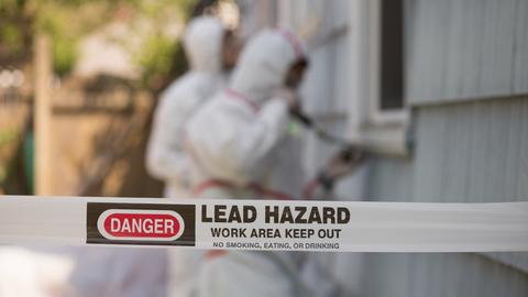 Tap reading "danger, lead hazard" in foreground with lead removal experts in background