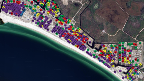 Drone image of a coastline with colorful dots showing types of damage, with the majority marked as "destroyed"