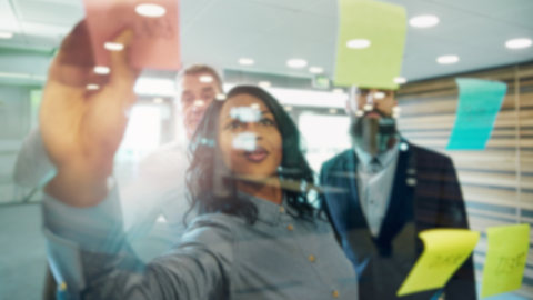 Woman putting a post-it note on a wall qhile brainstorming with her team