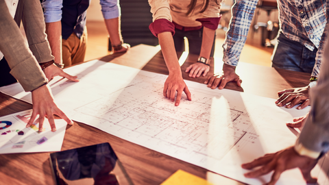 People bent over a desk discussing blueprint plans