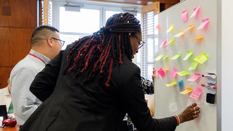 Diverse group of people adding post-it notes to a whiteboard at front of room