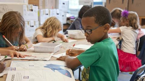 Diverse group of children at desks writing in school