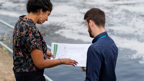 A male and female engineer looking at plans above a river and dam