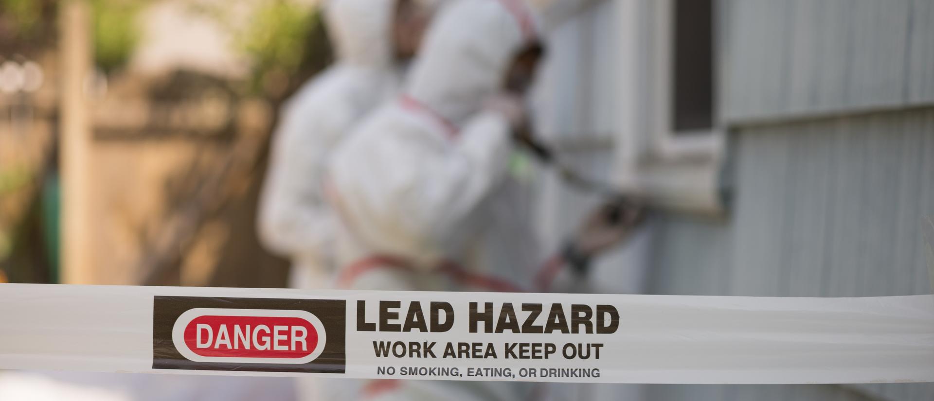 Tap reading "danger, lead hazard" in foreground with lead removal experts in background