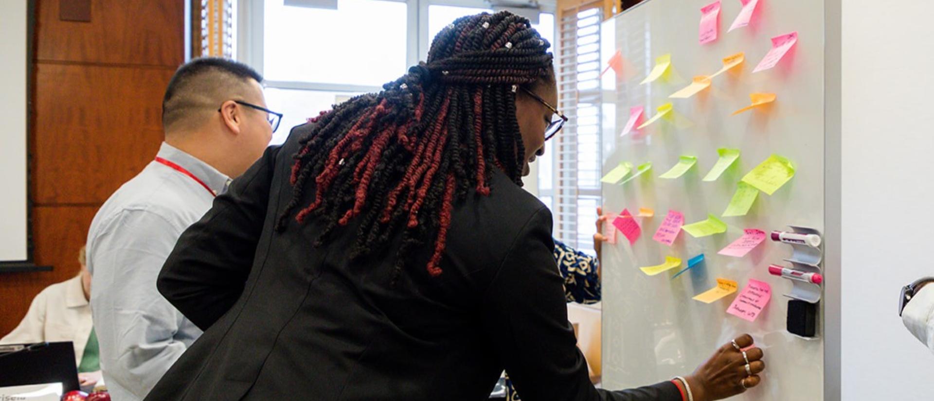 Diverse group of people adding post-it notes to a whiteboard at front of room