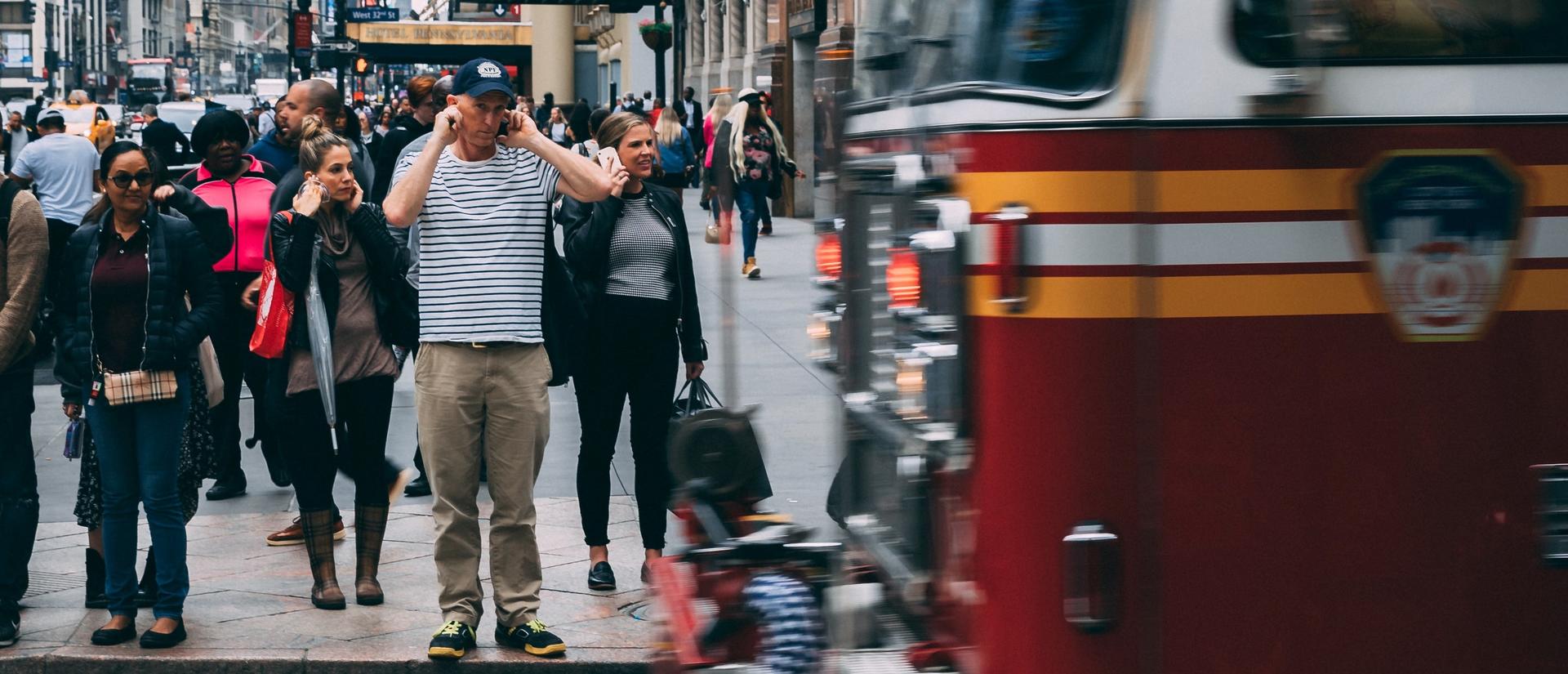 Fire truck driving by a crowd of people blocking their ears on the sidewalk